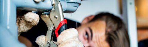 A plumber wearing gloves tightens a pipe connection under a kitchen sink using pliers, ensuring a secure plumbing repair in a Dallas home.