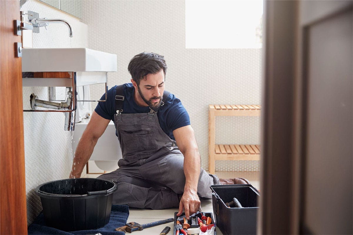 Plumber repairing a hidden water leak under a bathroom sink in a Dallas home