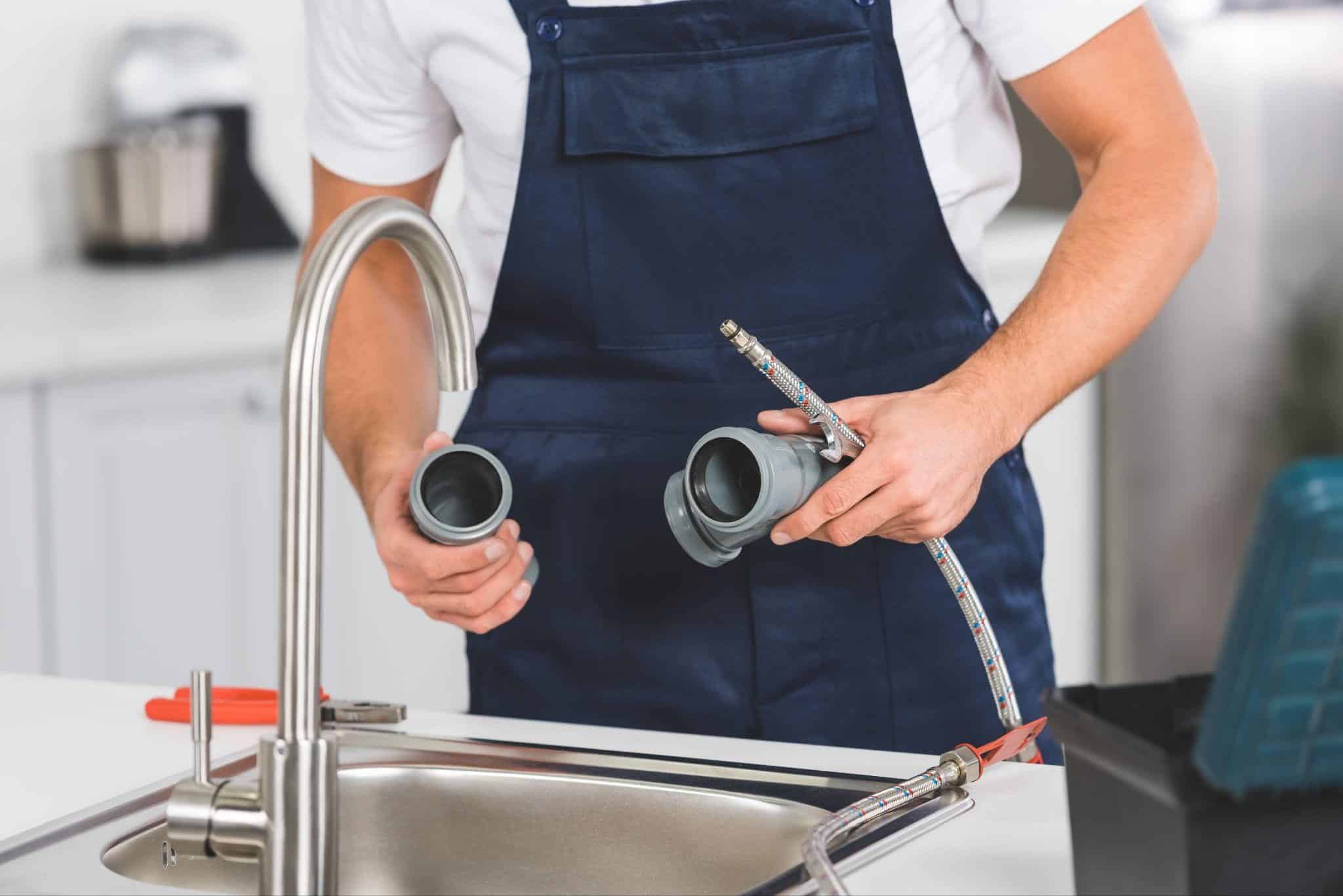 Plumber holding pipe fittings and braided hose during kitchen plumbing services repair