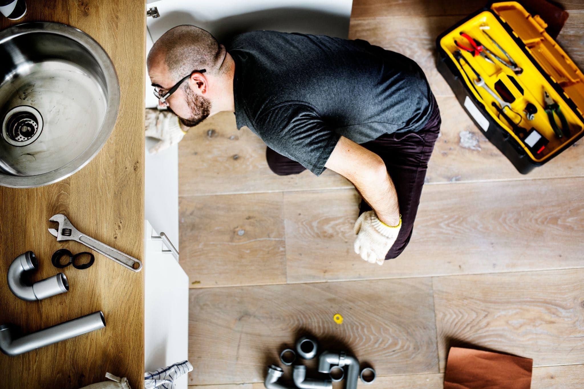 Plumber working under kitchen sink with tools during residential plumbing repair in Dallas