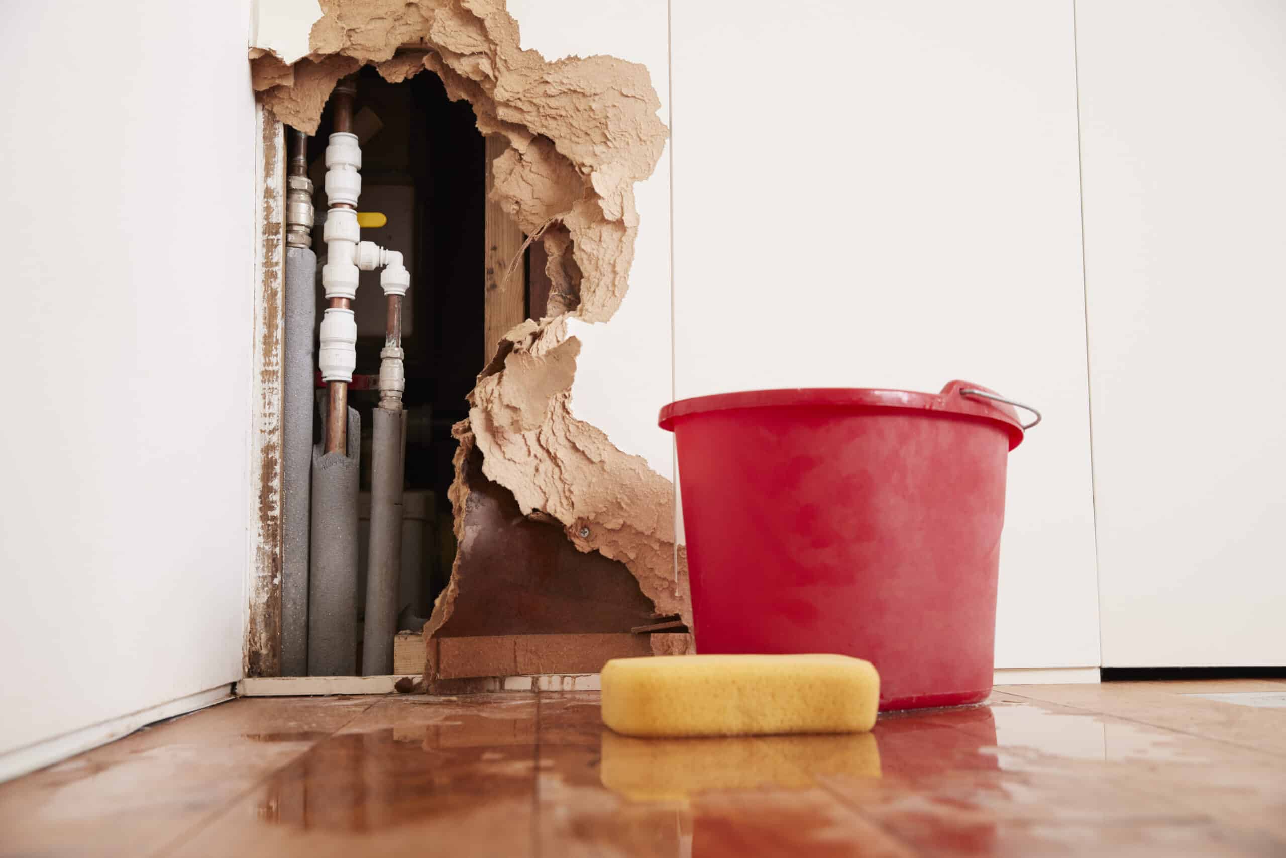 Interior water damage with bucket and exposed pipes, showing signs of a slab leak and why North Texas clay soil slab leaks can lead to hidden plumbing issues.